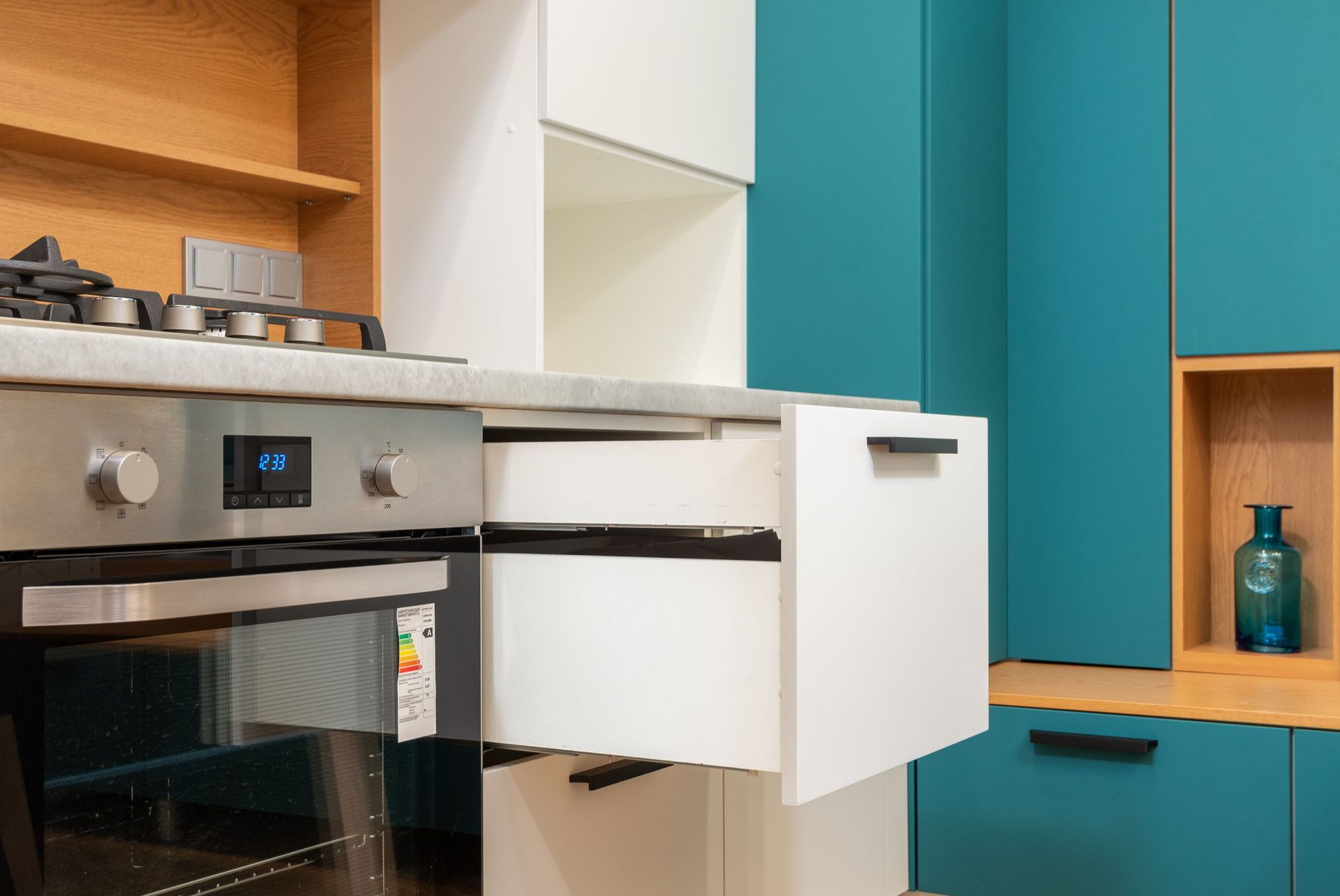 Contemporary oven with sticker and gas stove under wooden shelves in kitchen with open drawer